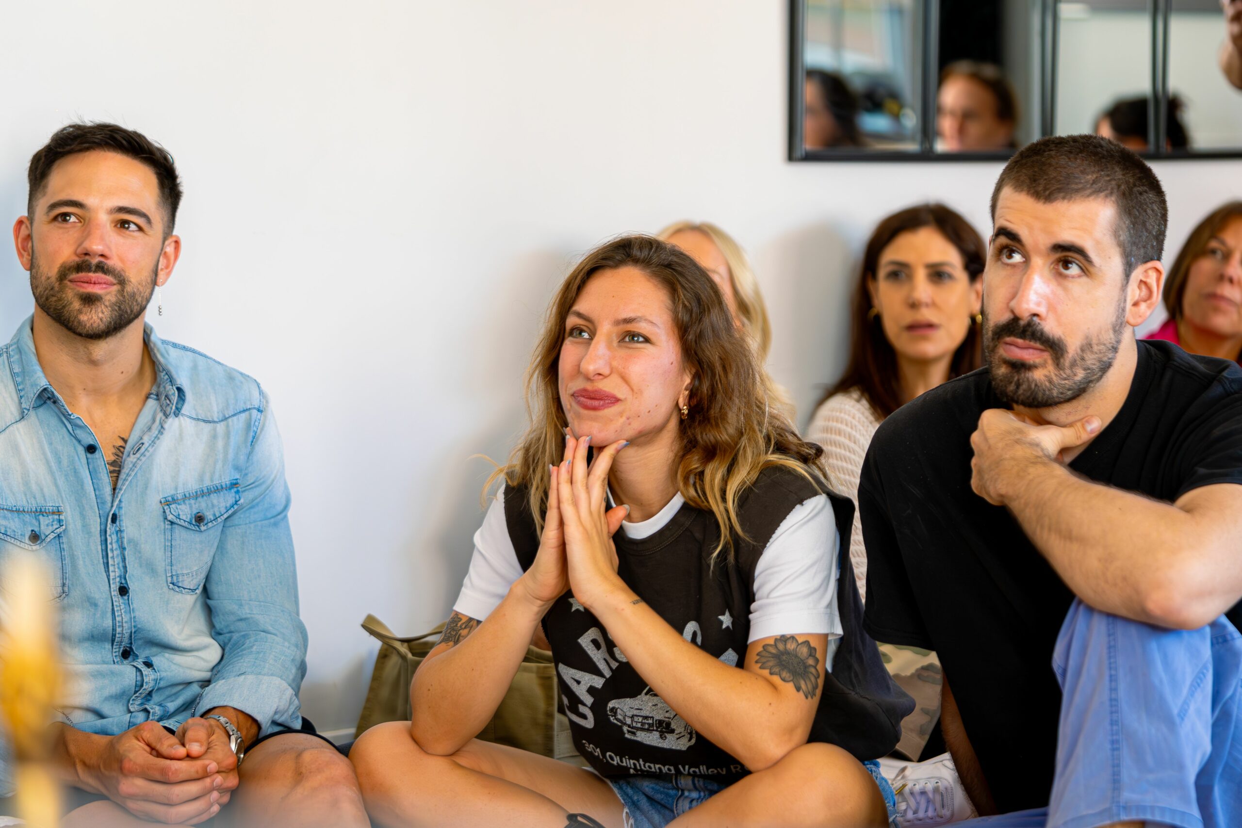 A group of adults attentively listening indoors, appearing engaged and smiling, creating a warm social scene.